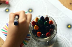 Mãos de criança colorindo o desenhos, remetendo a mudança escolar. 